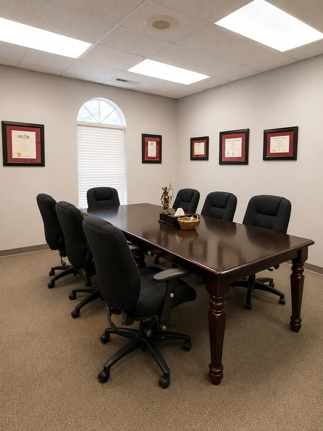 A professional mediation conference room with a polished table, black chairs, window, and framed certificates.